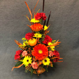 Autumn floral arrangement with gerbera daisies, carnations, and a small pumpkin in a vase