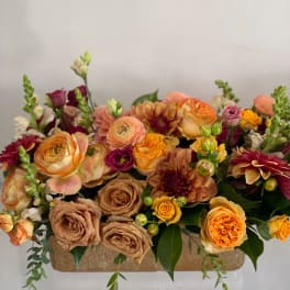 Mixed bouquet of peach, orange, and burgundy flowers in a rectangular container