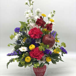 Mixed flower arrangement in a white pot with a "Teacher Ever" label