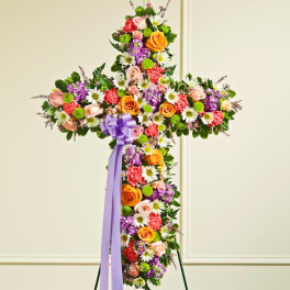Cross-shaped floral arrangement with roses, daisies, and a purple ribbon