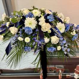 White and blue floral casket spray with ribbon on a coffin