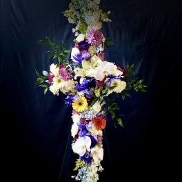 Tall cross-shaped standing spray with white lilies, orchids, mums and colorful daisies on a metal easel