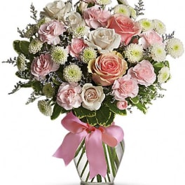Pink and white rose bouquet in a clear glass vase with a pink ribbon