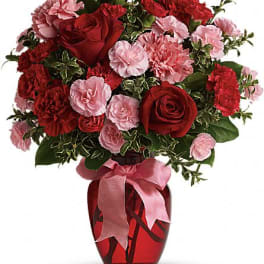 Red roses and pink carnations in a red vase with a pink ribbon