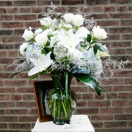 White lilies and roses in a glass vase with pale blue hydrangeas