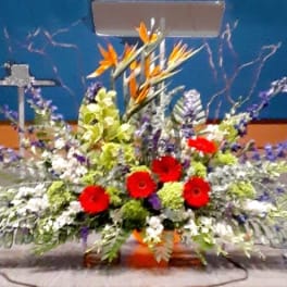 Large altar arrangement with red gerberas, orange birds of paradise, and purple flowers in a low container
