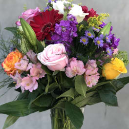 Mixed bouquet of roses, lilies, and purple flowers in a glass vase