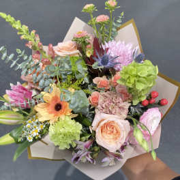 Handheld bouquet of mixed pink, peach, and green flowers wrapped in paper