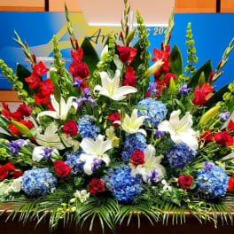 Large red, white, and blue stage floral spray with lilies, roses, gladiolus, and hydrangeas.