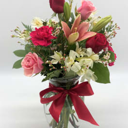 Mixed bouquet of roses, lilies, and carnations in a glass vase with a red ribbon
