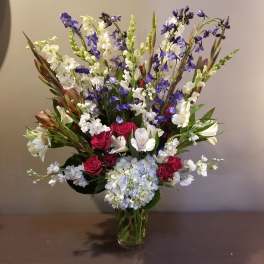 Tall bouquet of red roses, white lilies, blue flowers, and hydrangea in a glass vase