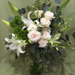 White roses and lilies in a glass vase with dark foliage
