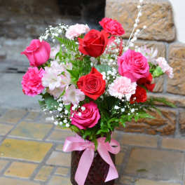 Pink and red roses with carnations in a vase tied with a pink ribbon.