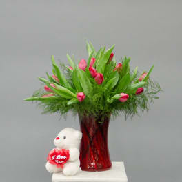 Pink tulips in a red glass vase with a small teddy bear holding a heart