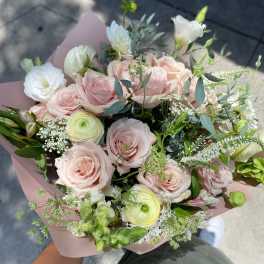 Handheld bouquet of pale pink roses and white blooms wrapped in blush paper