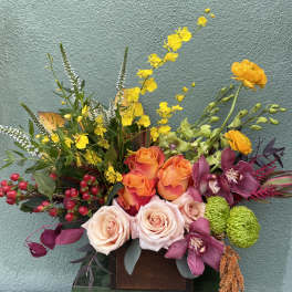 Colorful mixed flower arrangement with roses and orchids in a wooden container