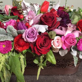 Mixed bouquet of roses, lilies, and pink blooms in a decorative container