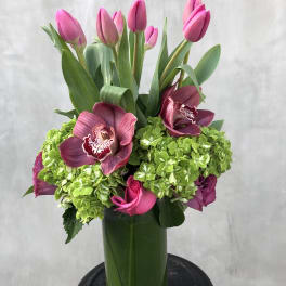 Pink tulips and magenta orchids arranged in a tall green vase