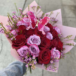 Bouquet of red and lavender roses with pink wrapping and a butterfly pick