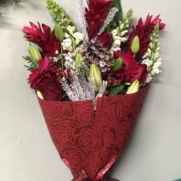 Red bouquet with lilies, roses, and silver accents wrapped in patterned paper