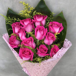 Bouquet of bright pink roses with dark green leaves and pink wrapping
