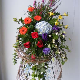 Tall mixed flower arrangement with roses, gerberas, and hydrangea in a wire stand