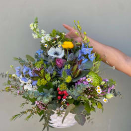 Mixed bouquet in a white basket with blue, yellow, pink, and white flowers