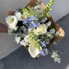 Bouquet of white calla lilies, blue flowers, and white roses wrapped in brown paper