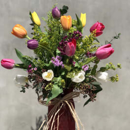 Colorful tulip bouquet in a red vase with raffia bow