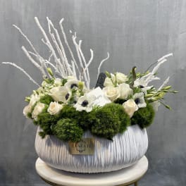 White floral arrangement in a large pleated vase with green accents