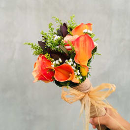 Handheld bouquet of orange calla lilies and roses with a burlap wrap and ribbon