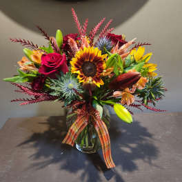 Mixed bouquet in a glass vase with sunflowers, roses, and lilies