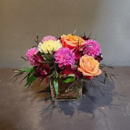 Mixed bouquet of pink, peach, and white flowers in a square glass vase