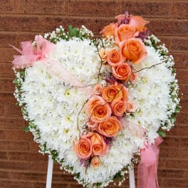 Heart-shaped floral spray with white chrysanthemums and peach roses on a stand