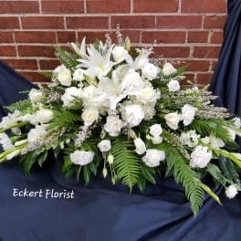 White funeral spray with lilies and roses on dark drape