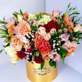 Mixed roses and pastel blooms arranged in a gold hatbox