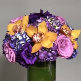 Bouquet of purple hydrangeas, yellow orchids, and pink roses in a glass vase