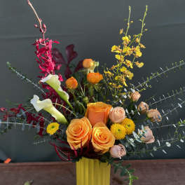 Mixed bouquet with orange roses, white calla lilies, and yellow blooms in a yellow vase