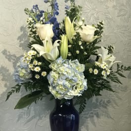 White lilies, roses, and blue flowers in a dark vase