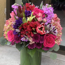 Bright mixed bouquet in a green glass vase with pink, purple, and red blooms