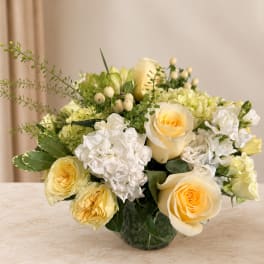 Cream and white rose bouquet in a glass vase with green accents
