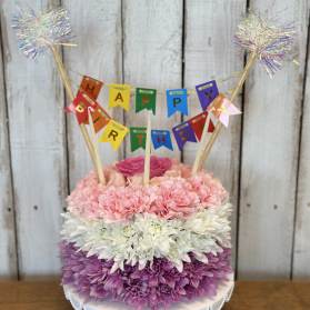 Birthday cake made of pink, white, and purple flowers with a banner topper