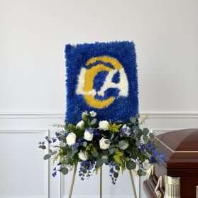 Blue and yellow floral funeral tribute on an easel beside a casket