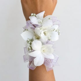 White floral wrist corsage with lavender ribbon on an arm