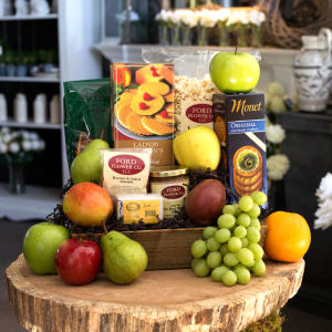 Gift basket of assorted fresh fruit and gourmet snacks on a rustic wooden slab.