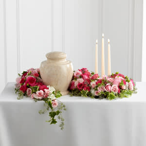Pink rose arrangements around a beige urn with three taper candles