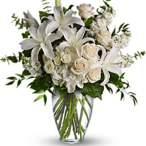 White lilies and roses arranged in a clear glass vase