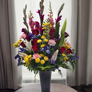 Tall mixed bouquet of roses, lilies, and colorful filler flowers in a purple vase