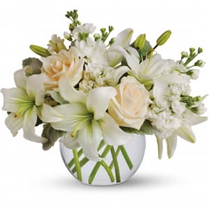 Low white lily and cream rose arrangement in a round clear glass vase with visible green stems.