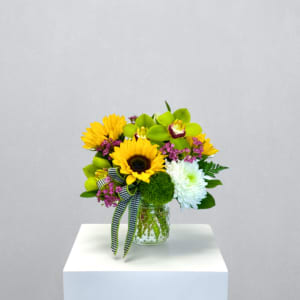 Short bouquet of sunflowers, green orchids, and white mum in a glass jar with checked ribbon.